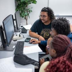 Three students sharing a computer and discussing school work.