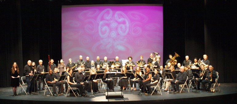 Captial City band performers posed for a group shot on the turner auditorium stage with a purple background behind them.