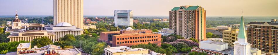 Ariel photo of Tallahassee downtown at sunset. Buildings are shown in a golden glow and car lights shine in the streets between them.